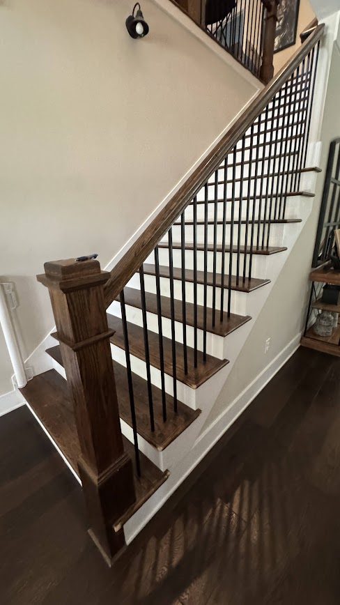 Finished dark-stained hardwood stair treads with wrought iron balusters