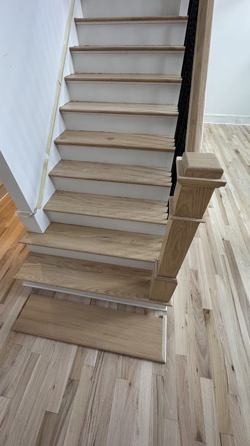 New hardwood stair treads being installed next to a matching hickory-look floor