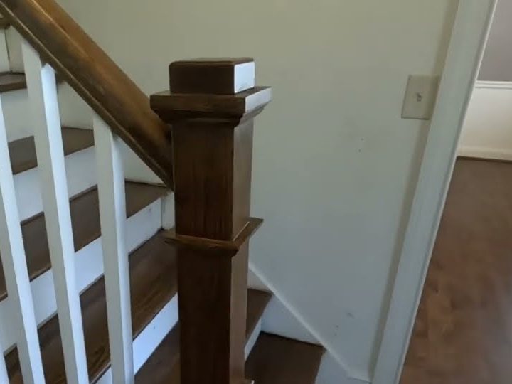 Stained box newel post and white square balusters beside a dark hardwood floor, staircase replacement in Roswell, GA