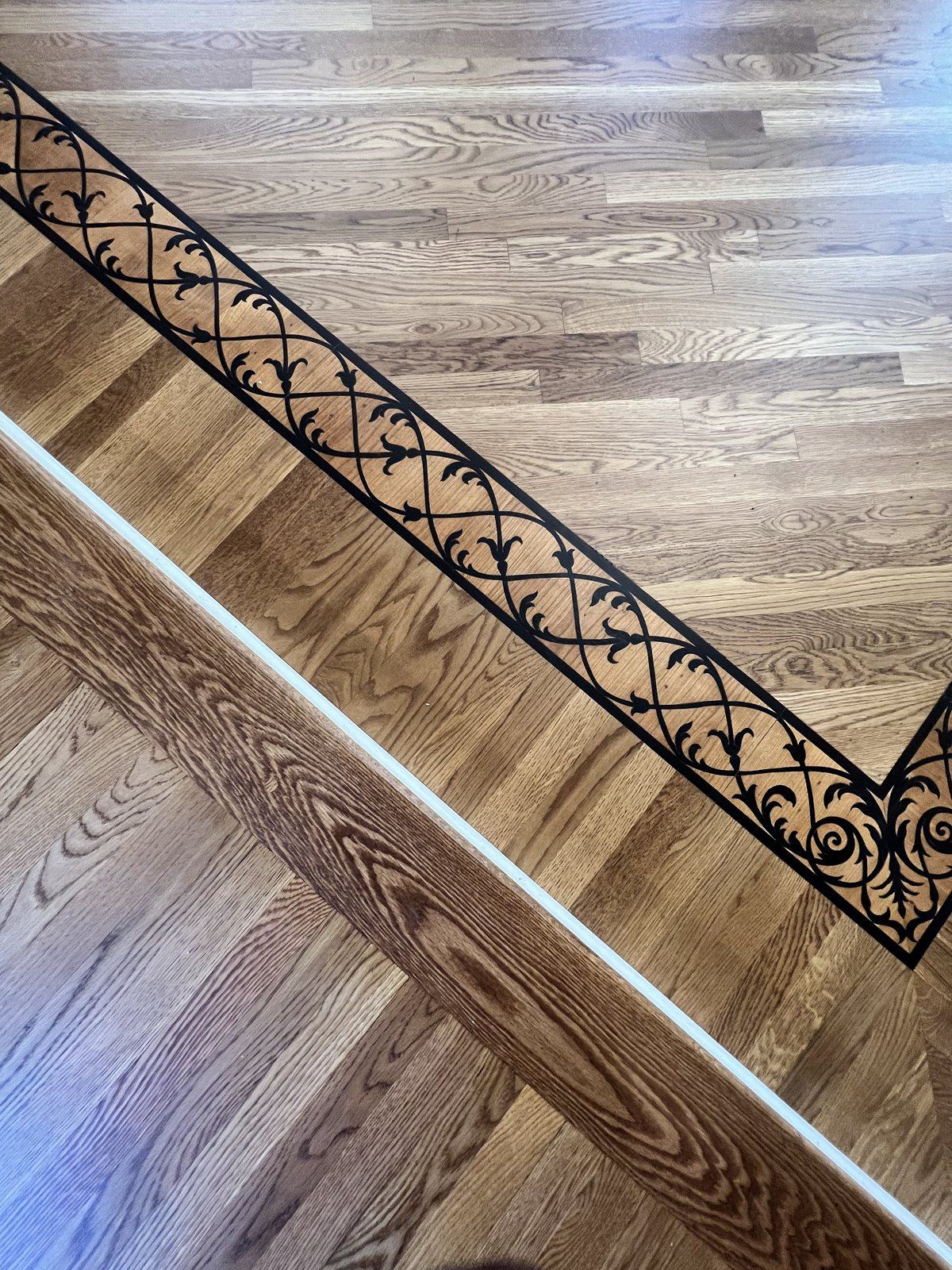 Close-up of a decorative wrought-iron scroll inlay border in a red oak hardwood floor, Golden Oak stain with matte finish