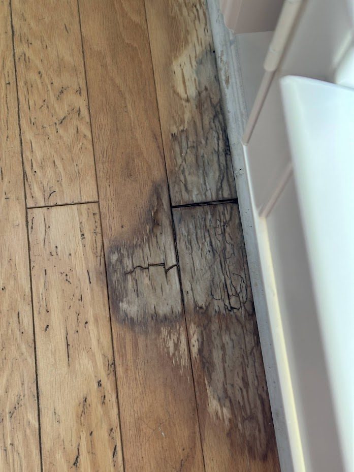 Close-up of blackened, cracked hardwood boards beside a cabinet where water pooled